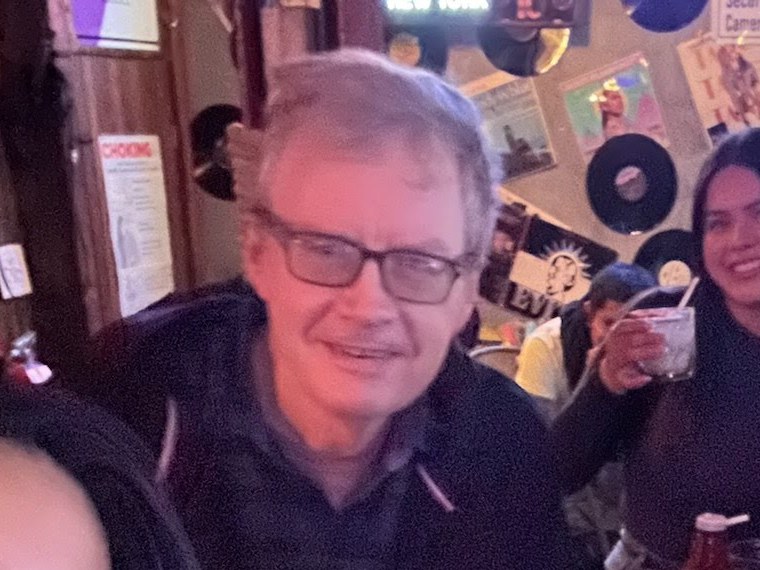 The Mentor at a wooden pub table under a wall of records